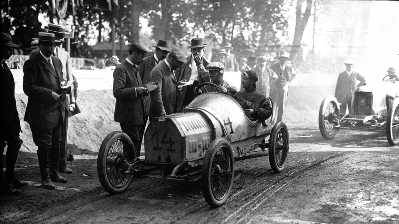 Ernest Friedrich in the Bugatti Type 13 fronts the starter at the 1911 French Grand Prix. Driving the smallest car in the race, Friedrichs finished the first lap in twelfth place. With a spate of crashes, lengthy pit stops for other competitors and retirements, the car slowly worked its way up the field, taking second place on the ninth lap and holding it until the finish. Near identical cars were sold by Bugatti until after WW1.