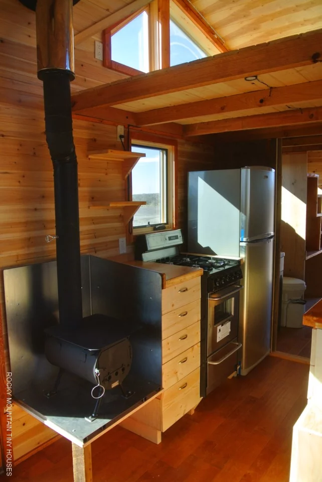 The interior includes a kitchen, lounge and dining area, with full-sized refrigerator, washer and dryer, and wood-burning stove (Photo: Rocky Mountain Tiny Houses)