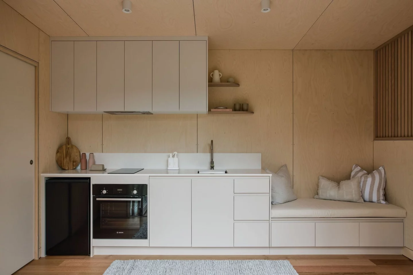 The Harper tiny house includes a spacious kitchen with an induction cooktop, cabinetry, and an adjacent storage-integrated sofa