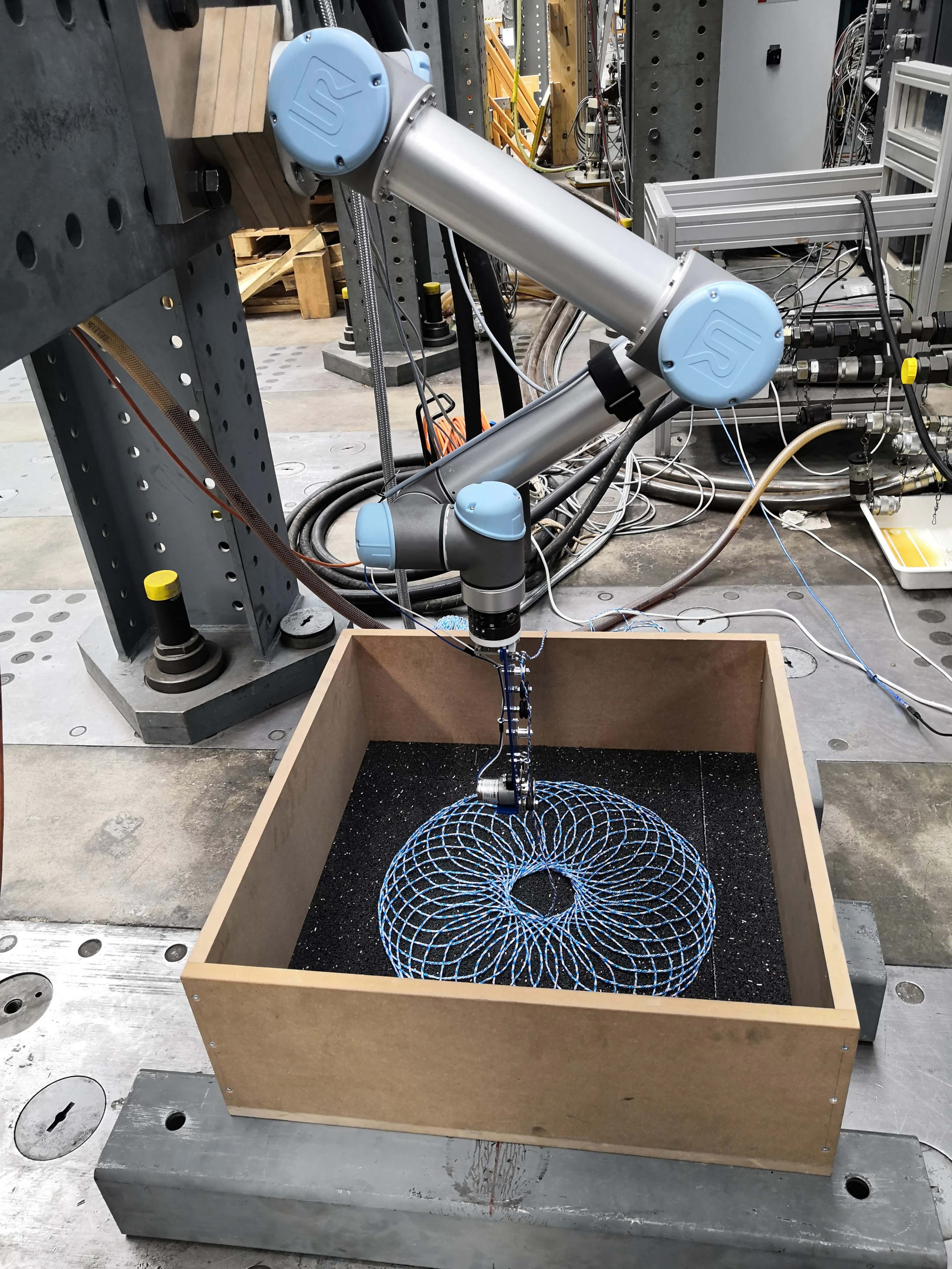 A robotic arm lays out a preprogrammed string pattern to reinforce the asphalt as part of road material research at Empa