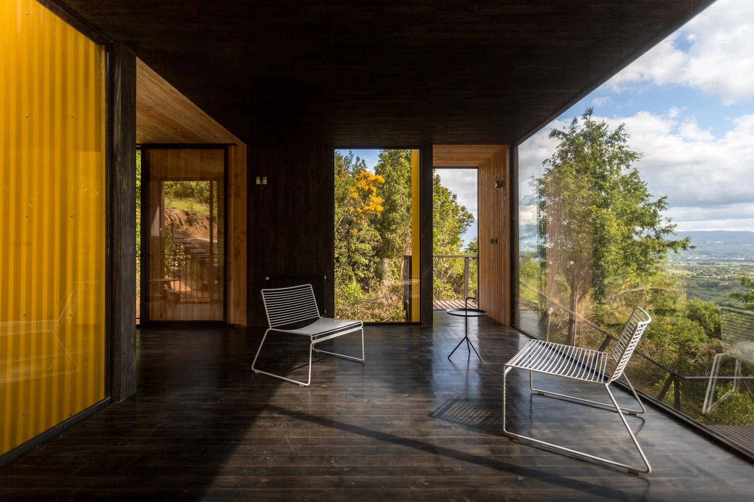 Large floor-to-ceiling glass windows are positioned throughout the entire home, offering stunning views of the surrounding forest landscape