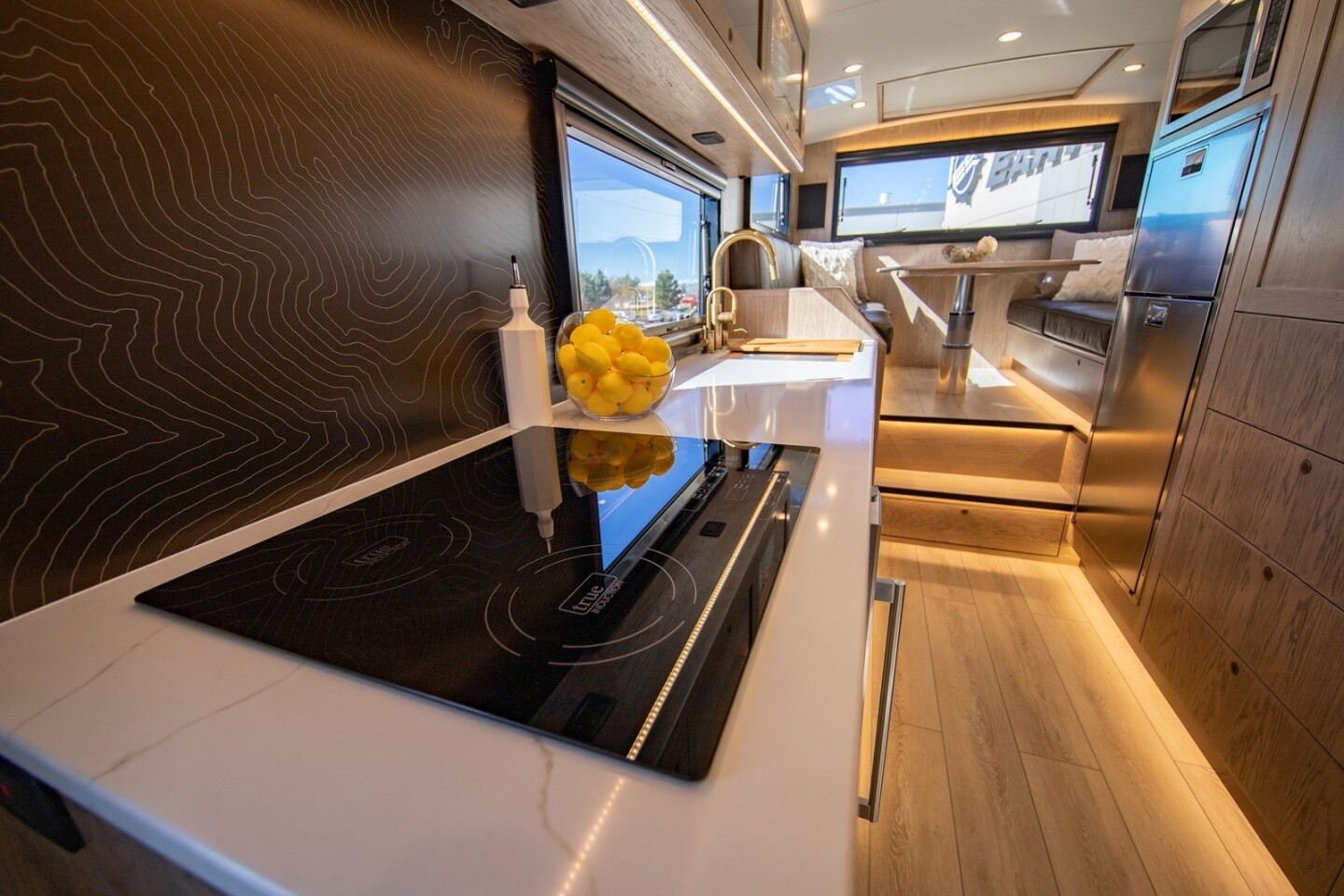 EarthRoamer shows off the long galley with topo-graphic backsplash, optional three-burner induction cooktop, stainless steel fridge and sink with available butcher block cover