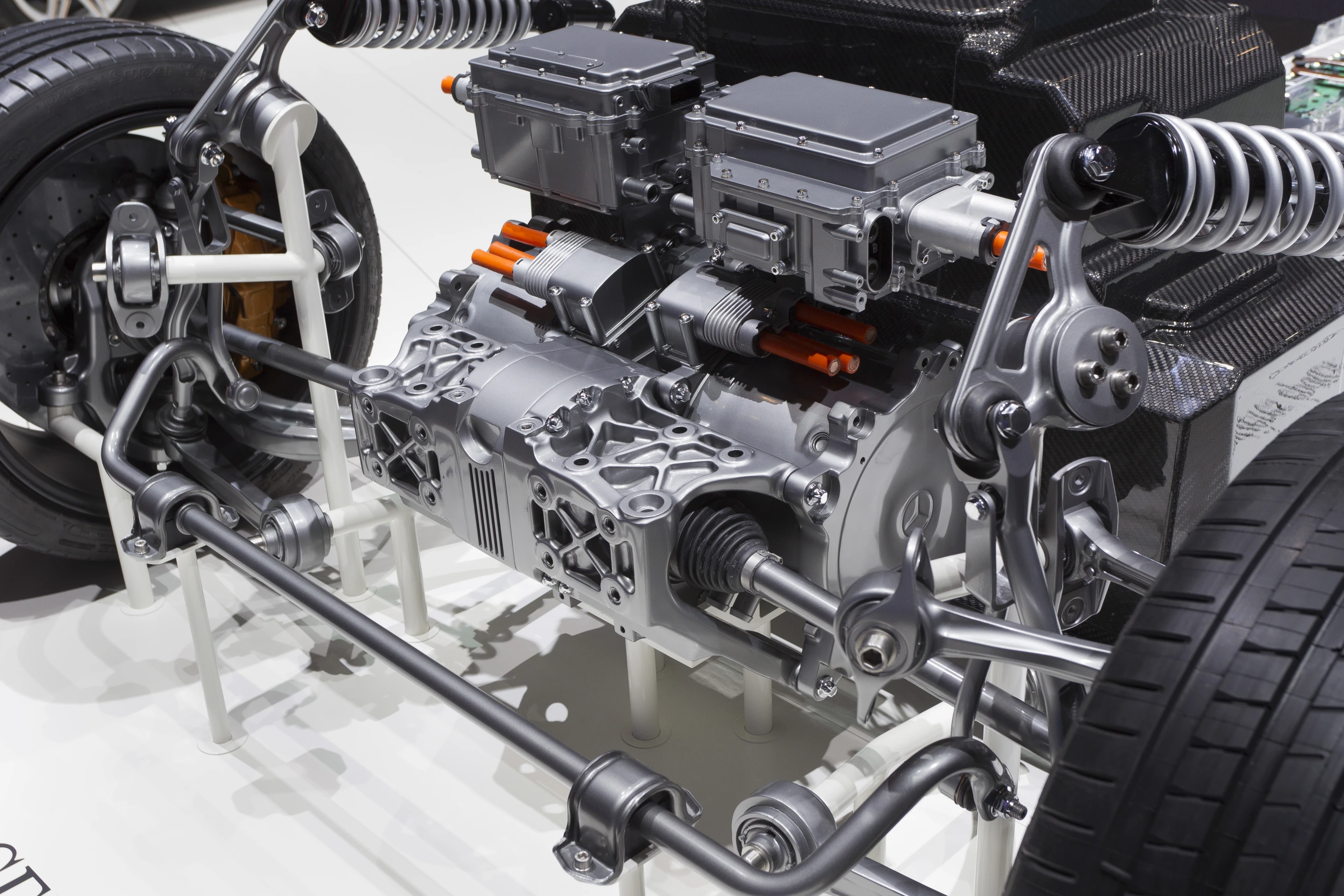 Mercedes-Benz SLS AMG E-CELL front end. Control electronics are at the top, motors, transmissions, and drive shafts appear below, and the multi-link front suspension at the bottom of the figure