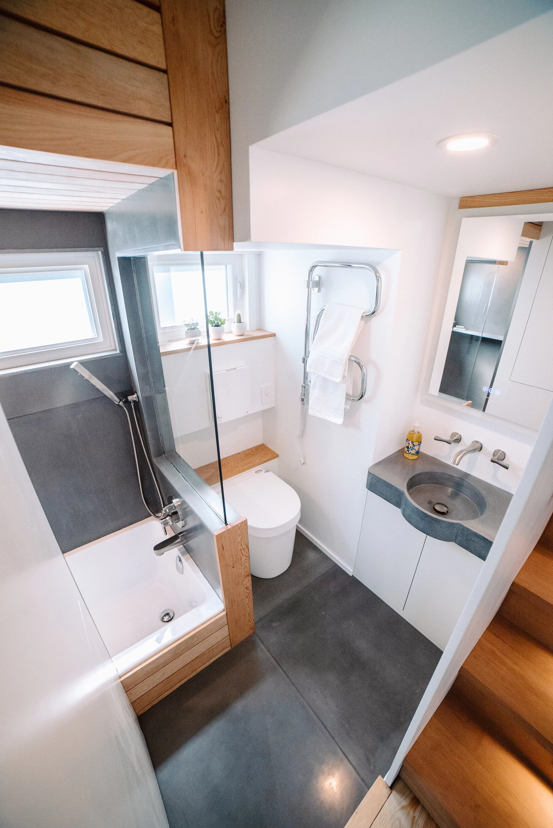 The Macdonald tiny house's bathroom includes a very small tub and shower, a concrete vanity sink, and a composting toilet