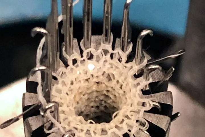 A circular knitting machine creates an artery graft out of a hybrid yarn