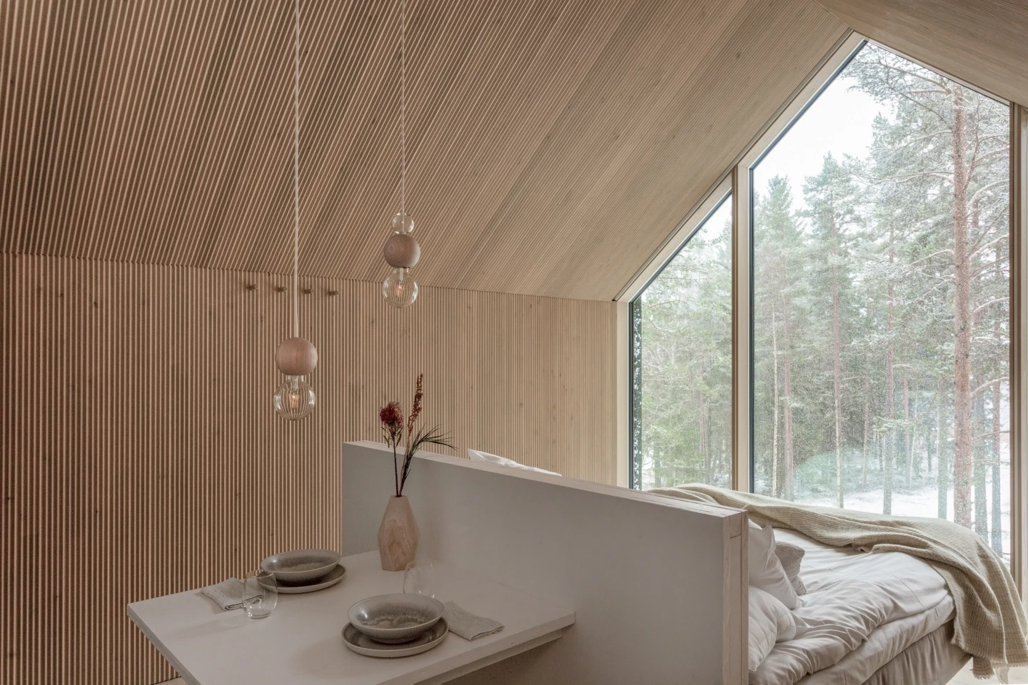 The bedroom is strategically positioned in front of the glass feature wall, allowing guests to enjoy the forest scenery while remaining warm and cozy in bed