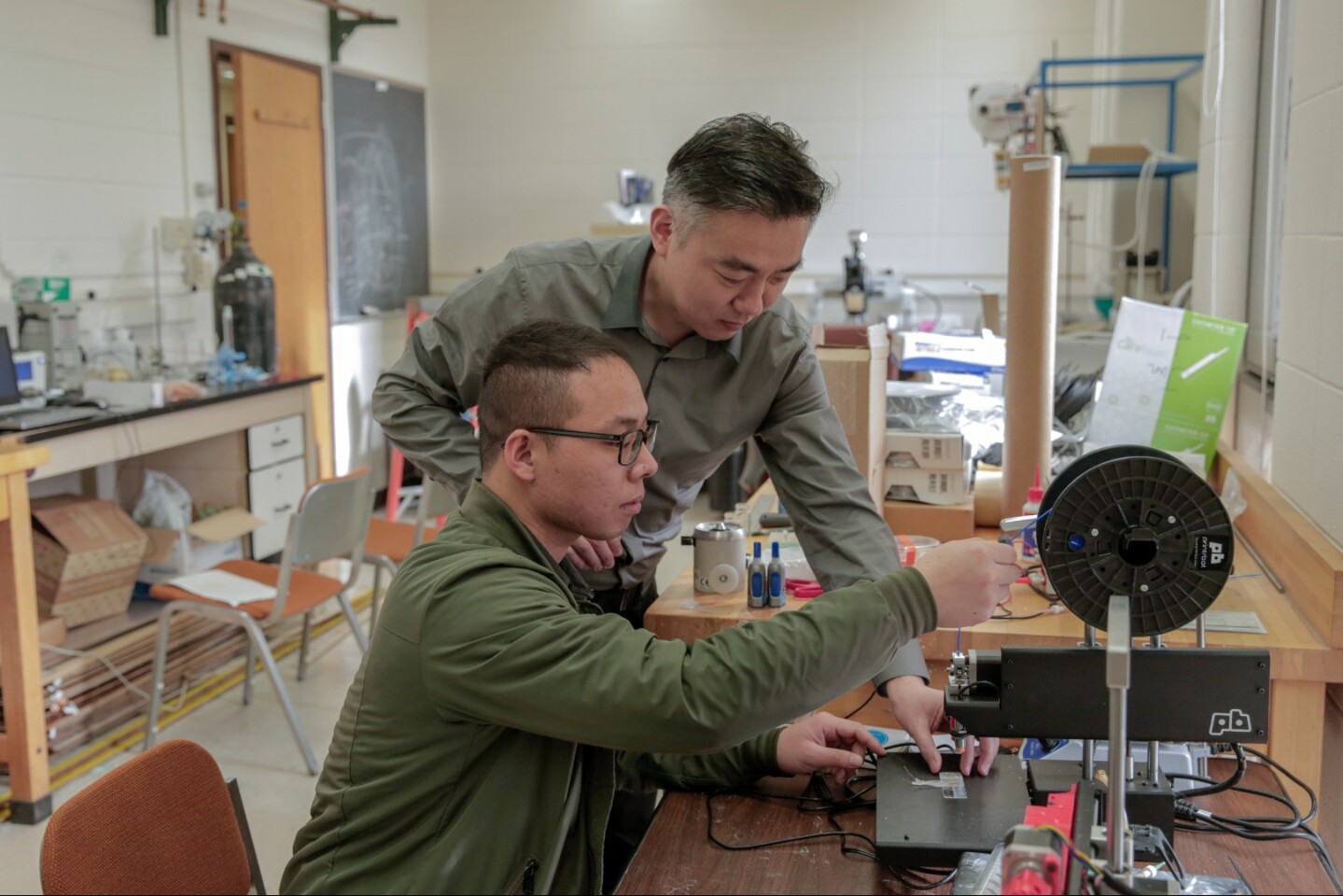 Graduate student Guang Yao (seated) uses a microscope to inspect the nanogenerators in the implantable weight-loss device