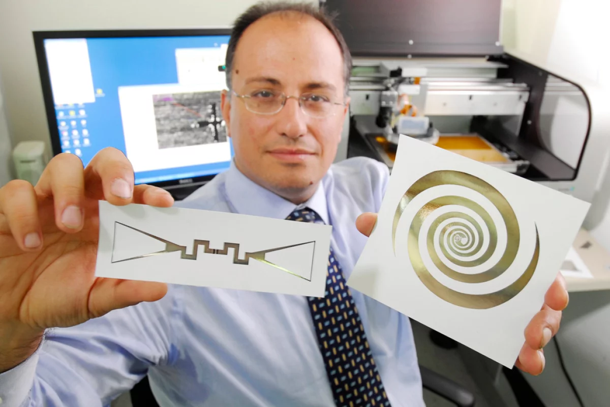 Manos Tentzeris holds a sensor (left) and an ultra-broadband spiral antenna for wearable energy-scavenging applications that were both printed on paper using inkjet technology (Image: Gary Meek)