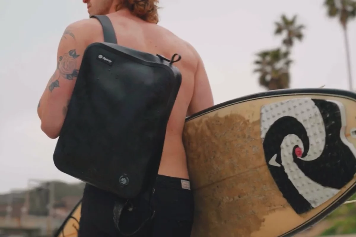 Shirtless surfer carrying bag and surfboard