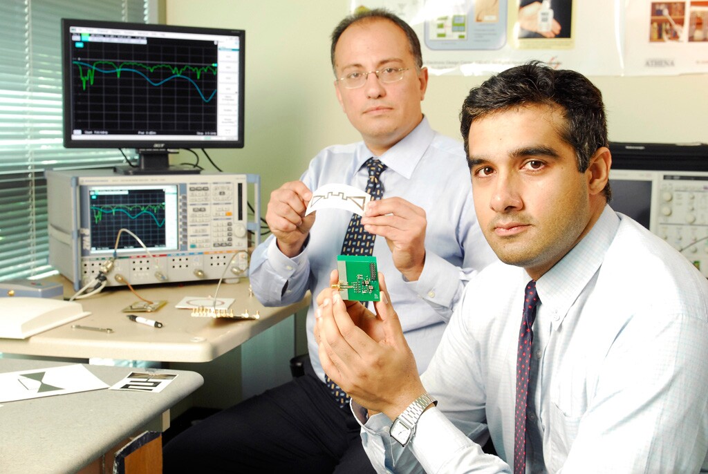 Georgia Tech graduate student Rushi Vyas (front) holds a prototype energy-scavenging device, while School of Electrical and Computer Engineering professor Manos Tentzeris displays a miniaturized flexible antenna (Image: Gary Meek)