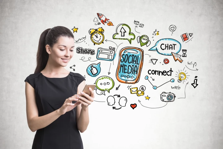 Beautiful young woman in a black dress looking at her smartphone screen. A gray wall background with a social media sketch