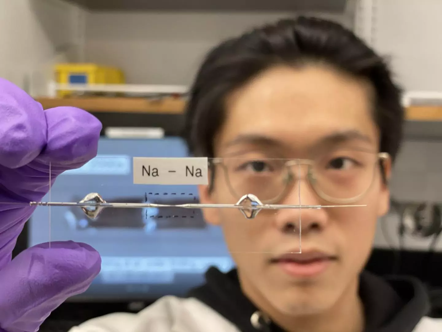 Researcher at Washington University in St Louis Bingyuan Ma holds up a transparent capillary cell, used to optimize the performance of an experimental sodium battery