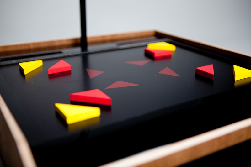 A child arranges corresponding colored blocks over the shapes. With the pieces in place, the "record" button is pressed, and the camera above, which points down at the screen, takes a snapshot