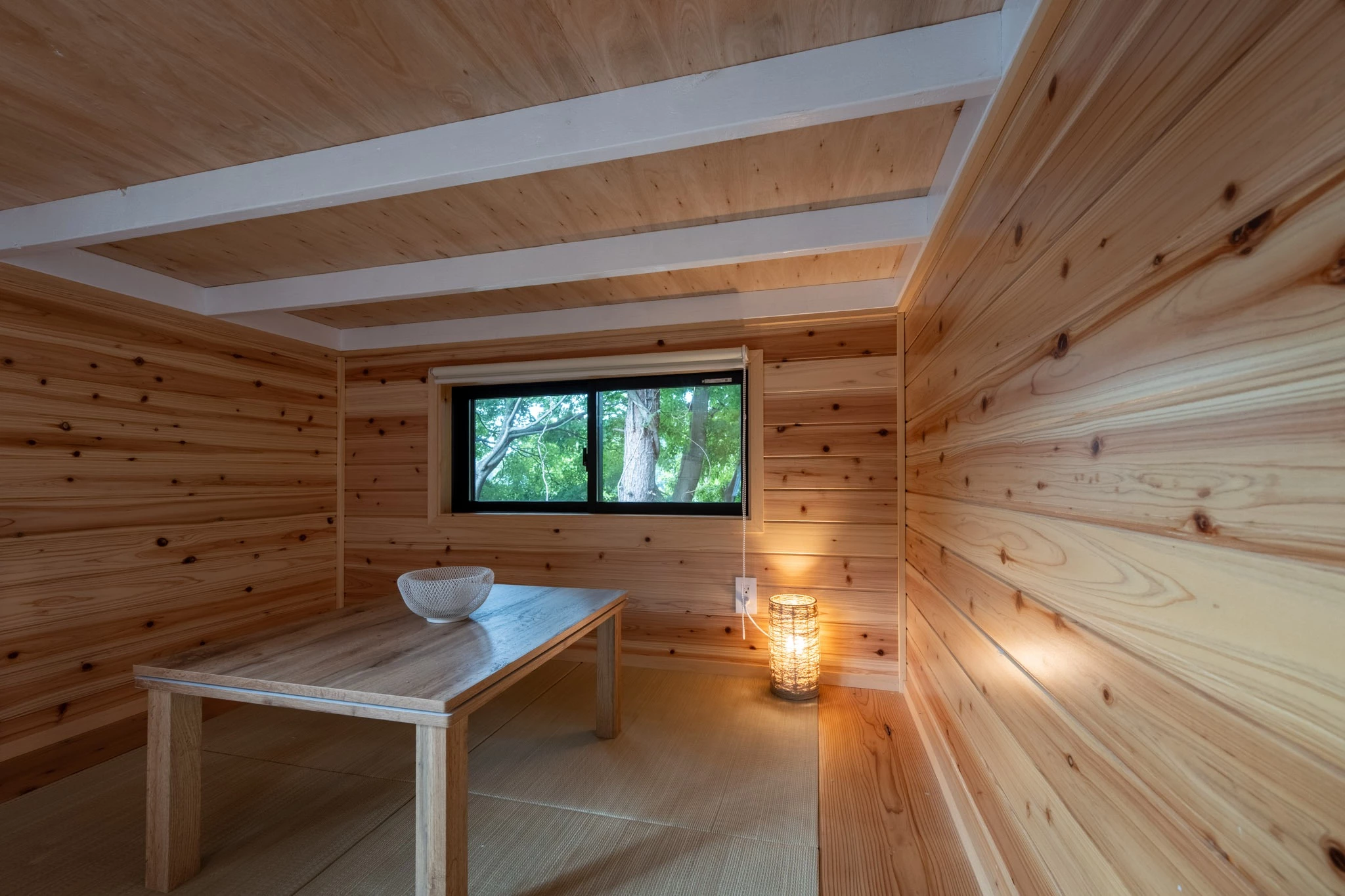 The Nozawa's living room has a low ceiling and includes straw matting on the floor and a dining table
