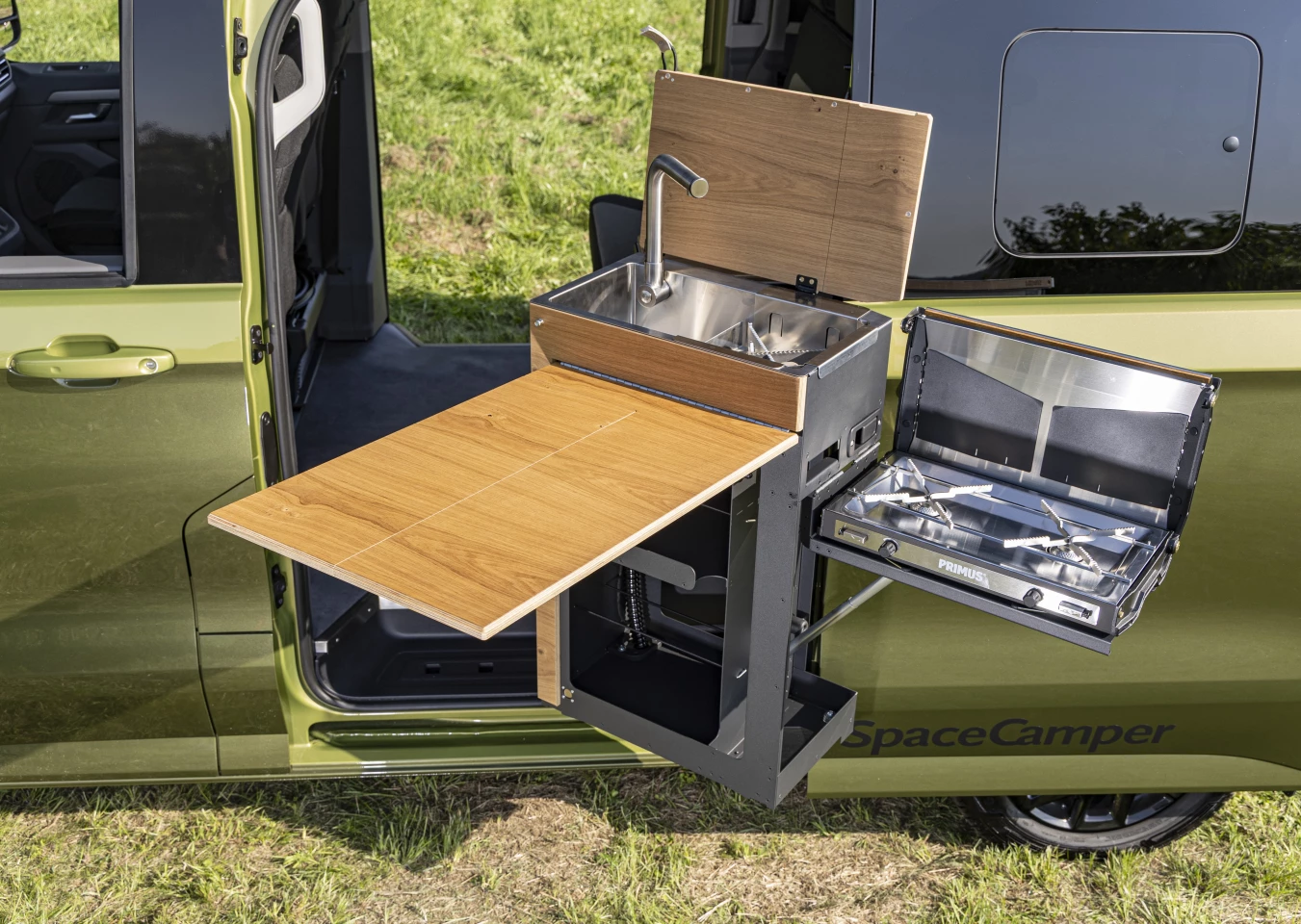 The kitchen features a flip-up worktop/face panel/dining table, flip-up dual-burner Primus stove, and a combo sink/single-burner stove with folding lid