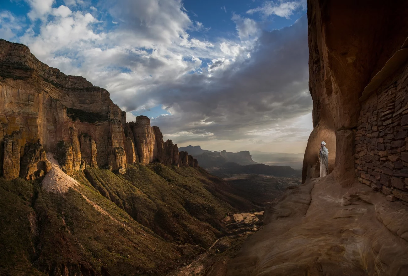 Siena Photo Awards. Honorable Mention - Journeys & Adventures. River. Tigray, Ethiopia. Priest Aregawi Wolde Mariam looks down at a dry river valley below an ancient church in Tigray.