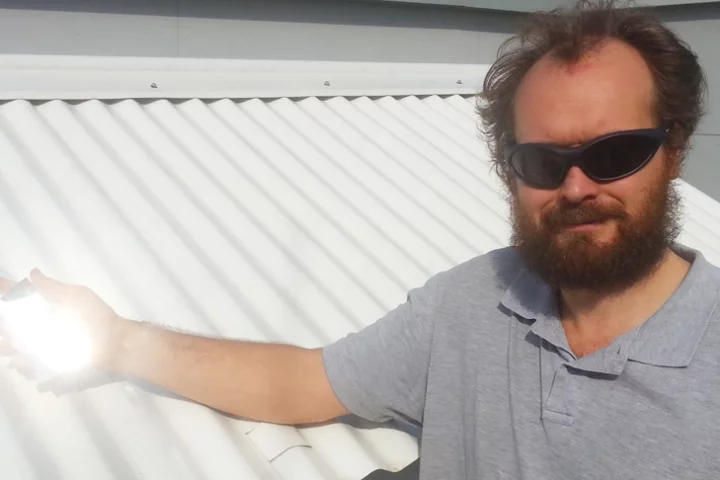 Dr Angus Gentle holding a piece of the special material over an existing cool roof used in testing