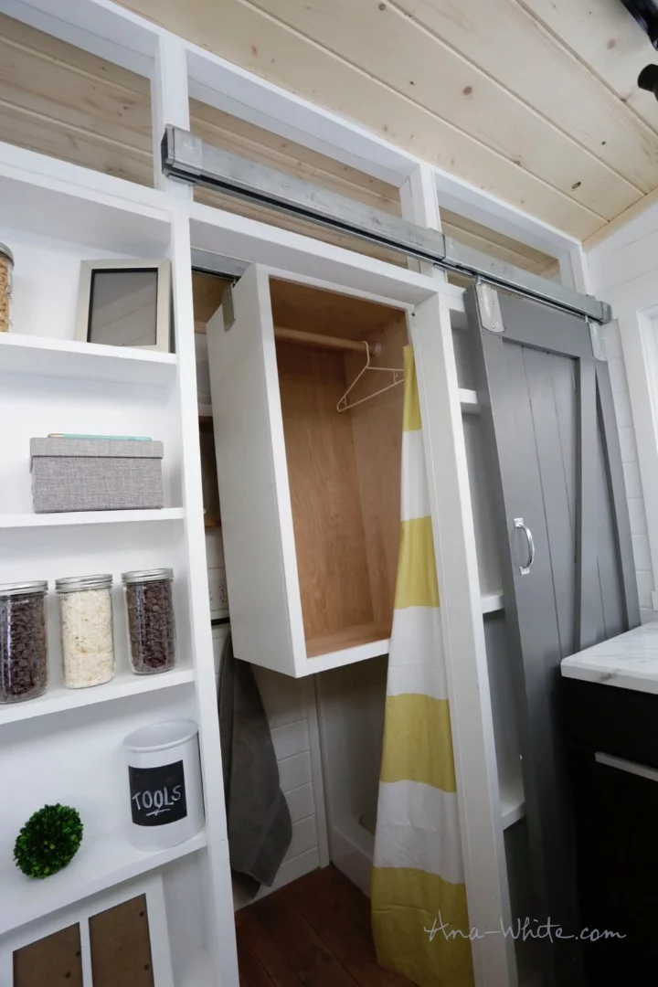 The Open Concept Rustic Modern Tiny House's bathroom includes a movable clothes closet on a track