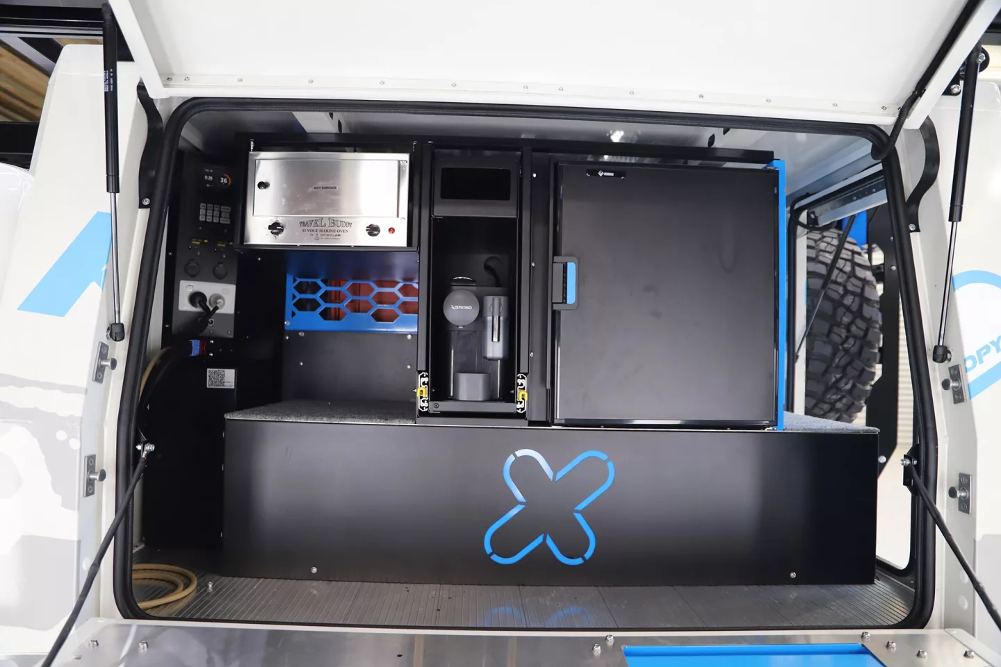 The passenger side of the canopy is dedicated to an available kitchen area with fridge/freezer on the right, coffeemaker in the center, electric oven top left/center, and electrical hardware on the left