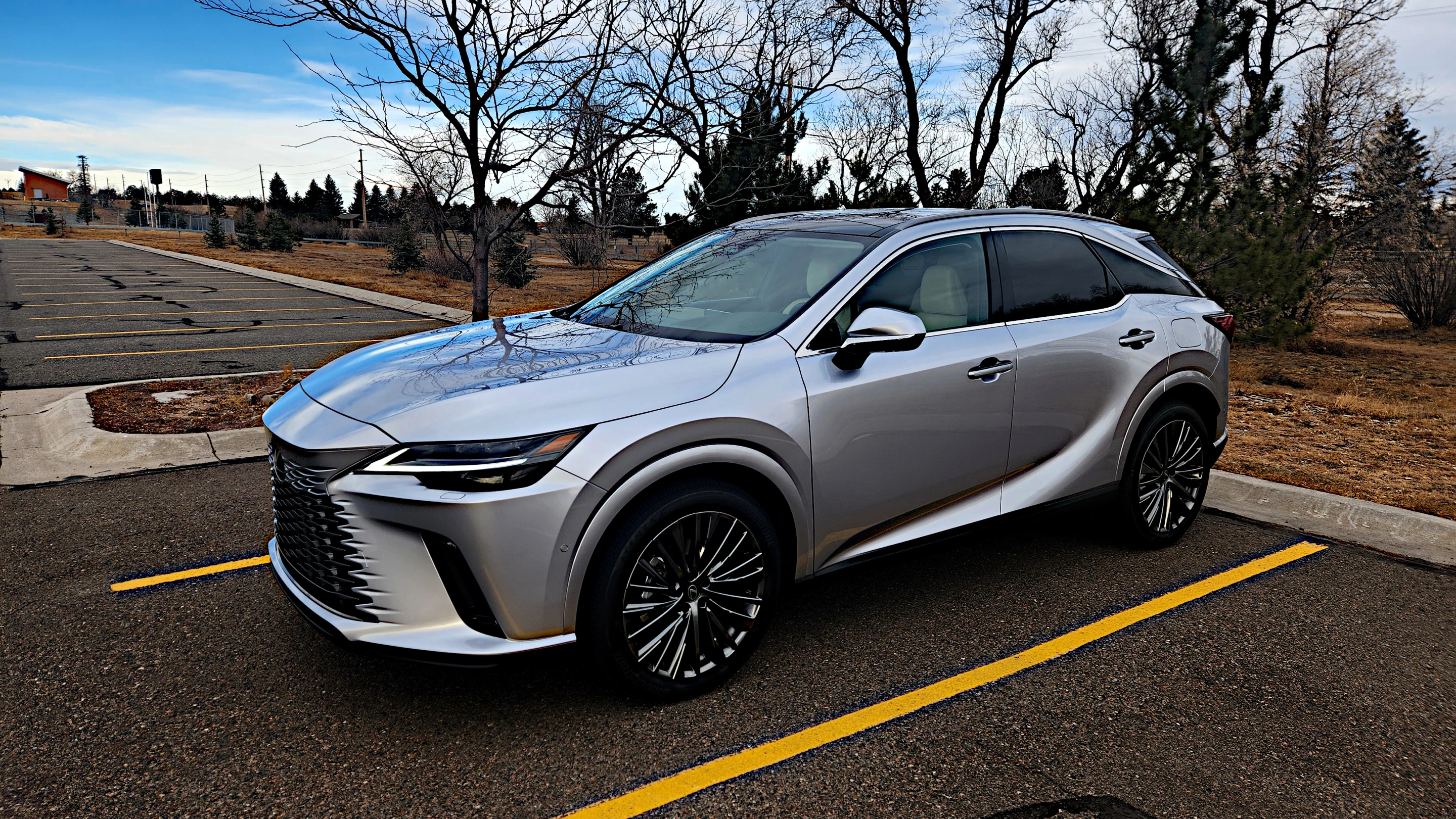 The 2026 Lexus RX 450h+ hybrid SUV finished in a premium metallic paint parked in a lush setting.