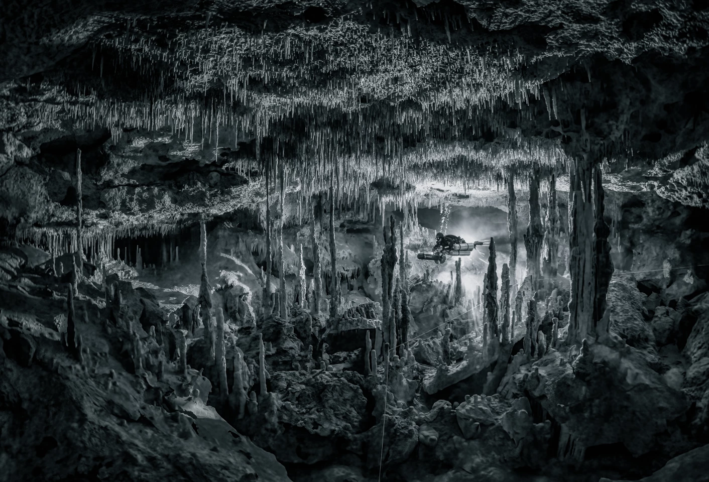 Labyrinth of Speleothems. A diver navigating his underwater scooter through a chamber full of stalactites and stalagmites, showing the raw nature and amazing textures of the flooded caves in Mexico.