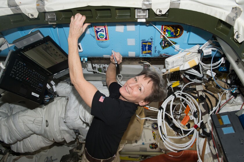 Peggy Whitson signing her name on an ISS bulkhead next to her expedition 50 crew patch
