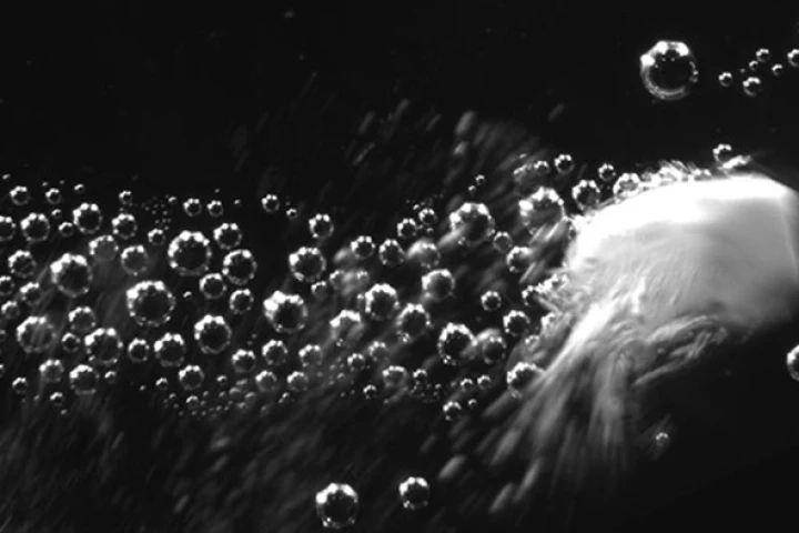 Image showing a carbonate particle releasing carbon dioxide and propelling at a high velocity through an aqueous solution