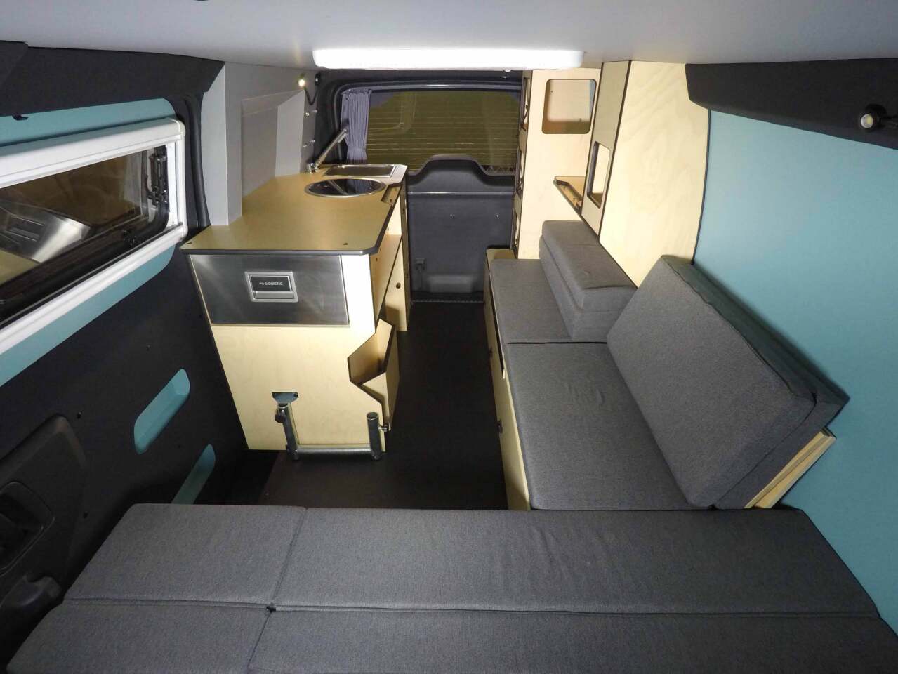 The Mobile Base Camp interior is filled out with an L-shaped sofa, storage shelving and a kitchen block