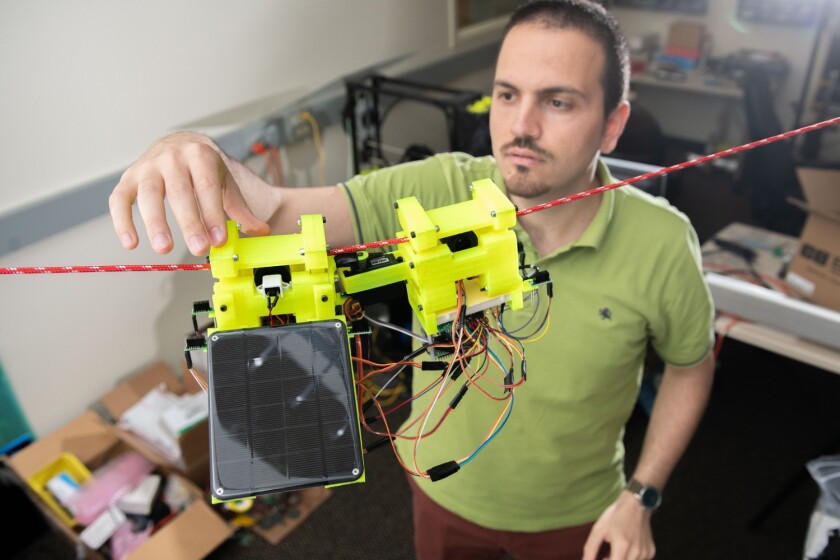 Consisting largely of 3D-printed gears and other parts, the SlothBot is designed to grip horizontally-strung cables with its battery-powered rubber wheels