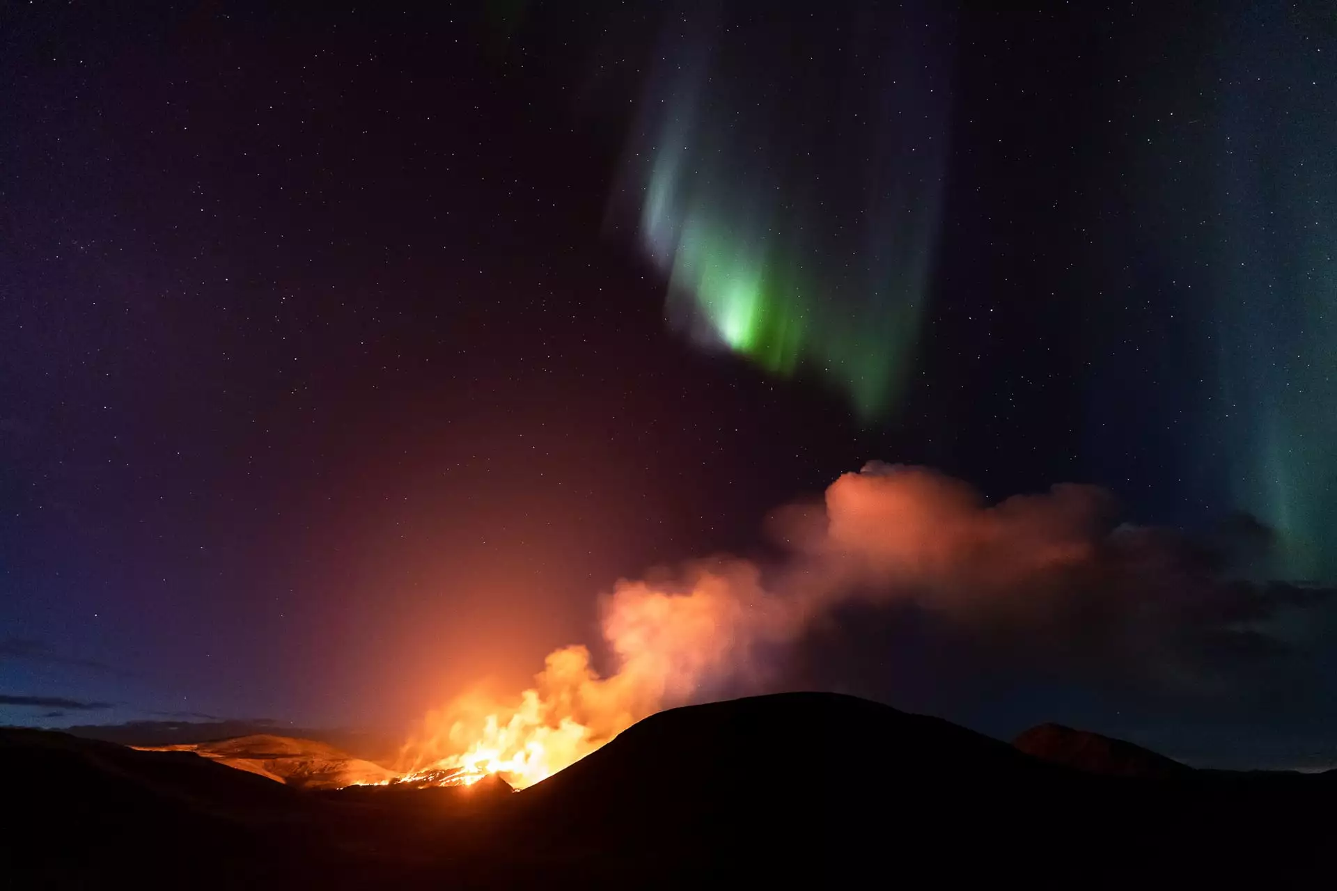 Volcanic Aurora Borealis by Jeroen Van Nieuwenhove, shot atop the Geldingadalir volcano in Iceland. The blue-green glow of the aurora overhead complements the yellow-orange of the erupting lava. The photographer almost gave up for the night due to cloud cover, before they eventually parted and the aurora brightened.