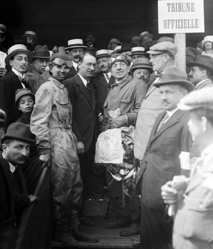 The riding mechanic and Ernest Friedrich (with winner's garland) flank Ettore Bugatti as they await the presentation of winners after the 1920 "VIII Coupe des Voiturettes"