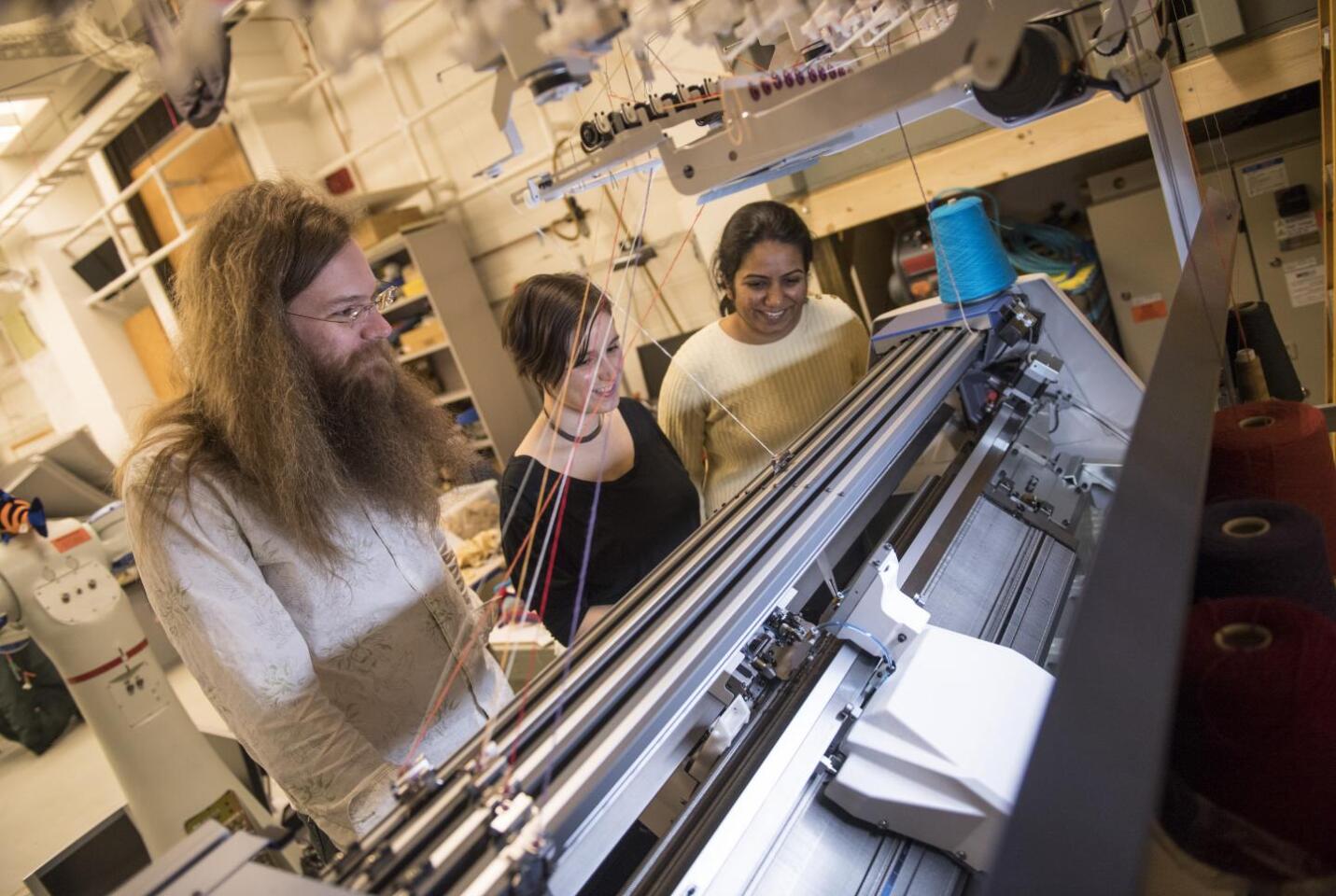 James McCann, Lea Albaugh and Vidya Narayanan watch a knitting machine work on a 3D shape