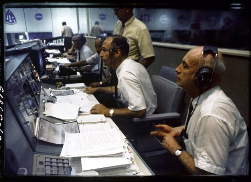 View of activity along a row of consoles during the Apollo 11 mission, as flight controllers watch astronauts Neil Armstrong and Buzz Aldrin walk on the surface of the Moon