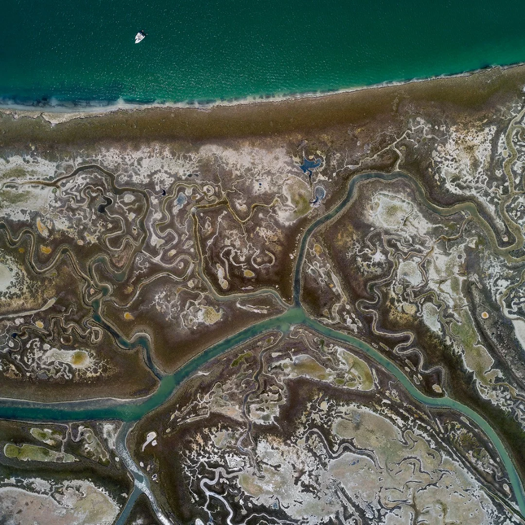 Picnic boats in front of the fascinating swirling tidal channels in the middle of the Venice lagoon seen from above