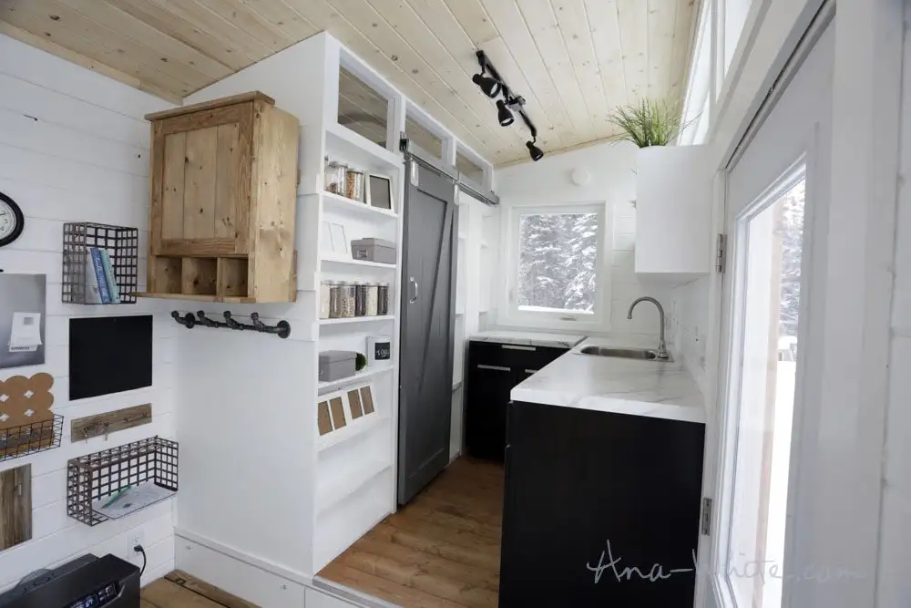 The Open Concept Rustic Modern Tiny House's raised kitchen area has storage space beneath