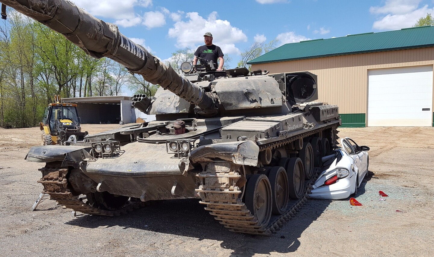 Standing atop the Chieftain FV4201 battle tank, the author surveys the machine's movement as journalist Tim Esterdahl pilots it over a hapless car