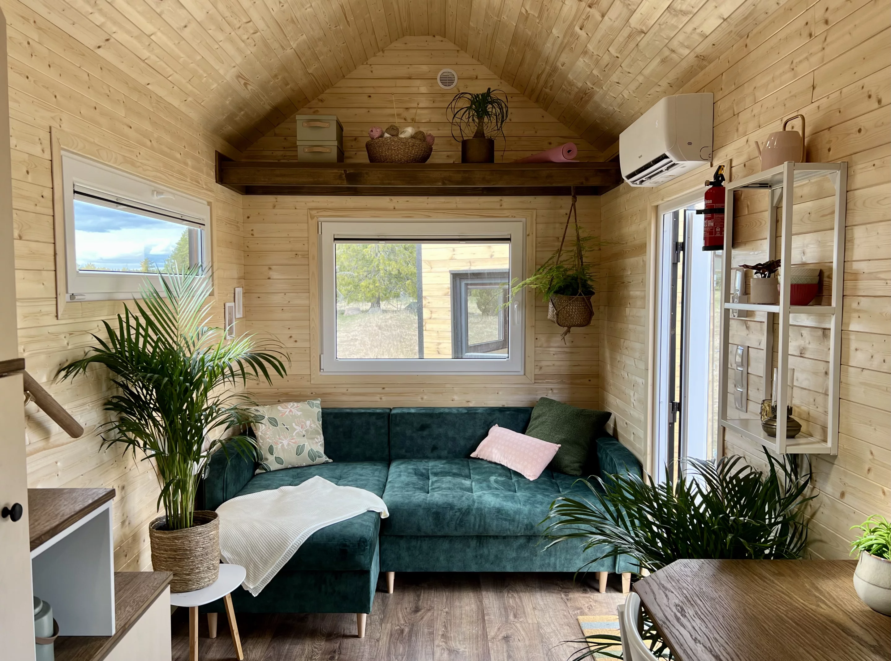 Visitors enter the Sunshine tiny house into the living room, which includes a sofa bed and some shelving. Heating and cooling comes from a small mini-split air-conditioning unit