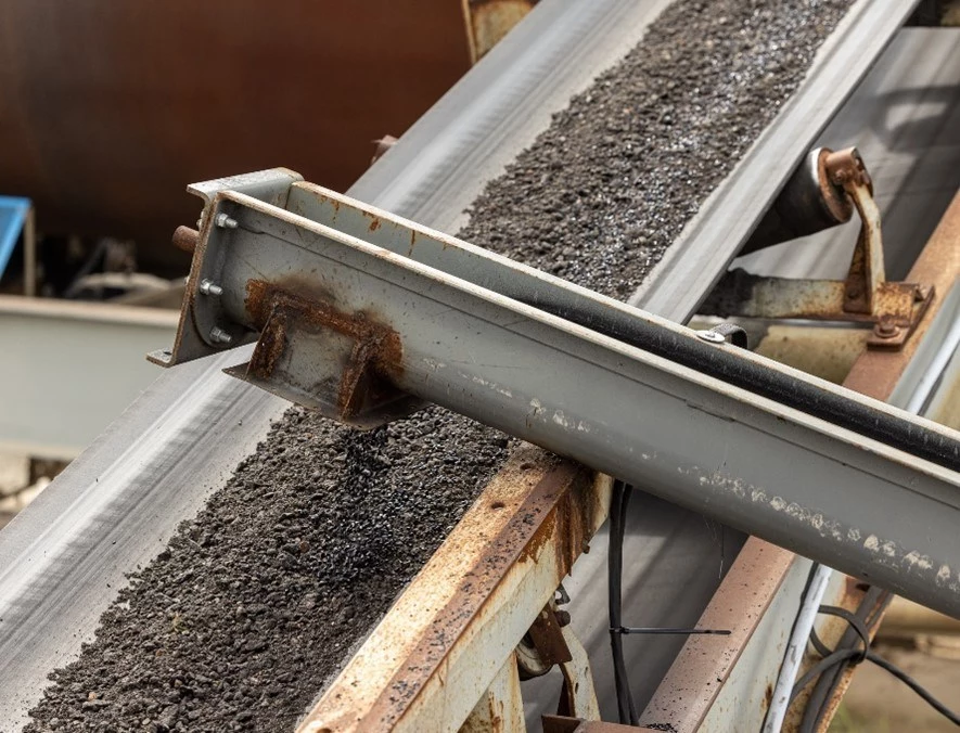 An auger (foreground) adds Recycled Toner Pellets to an asphalt mix on a feeder belt