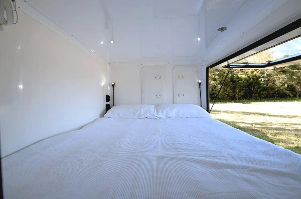 The cozy interior includes a queen bed, fan, lights and access to the front storage lockers