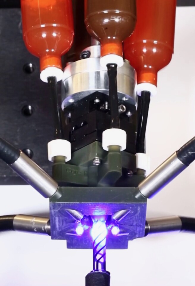 A rig used to generate filament. It has ink cartridges on top and rotating nozzles on the bottom.