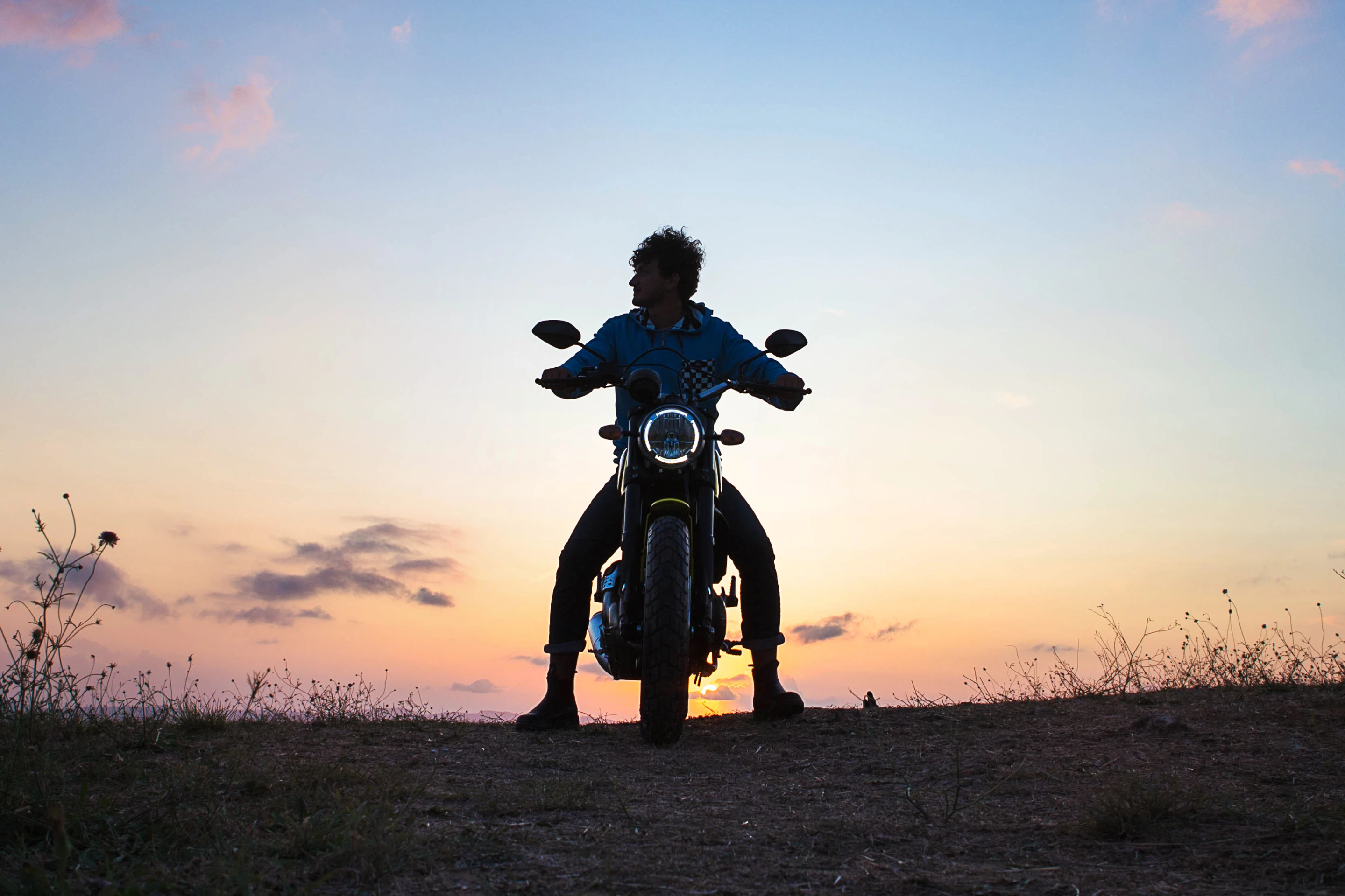Man sits on Ducati Scrambler at sunset