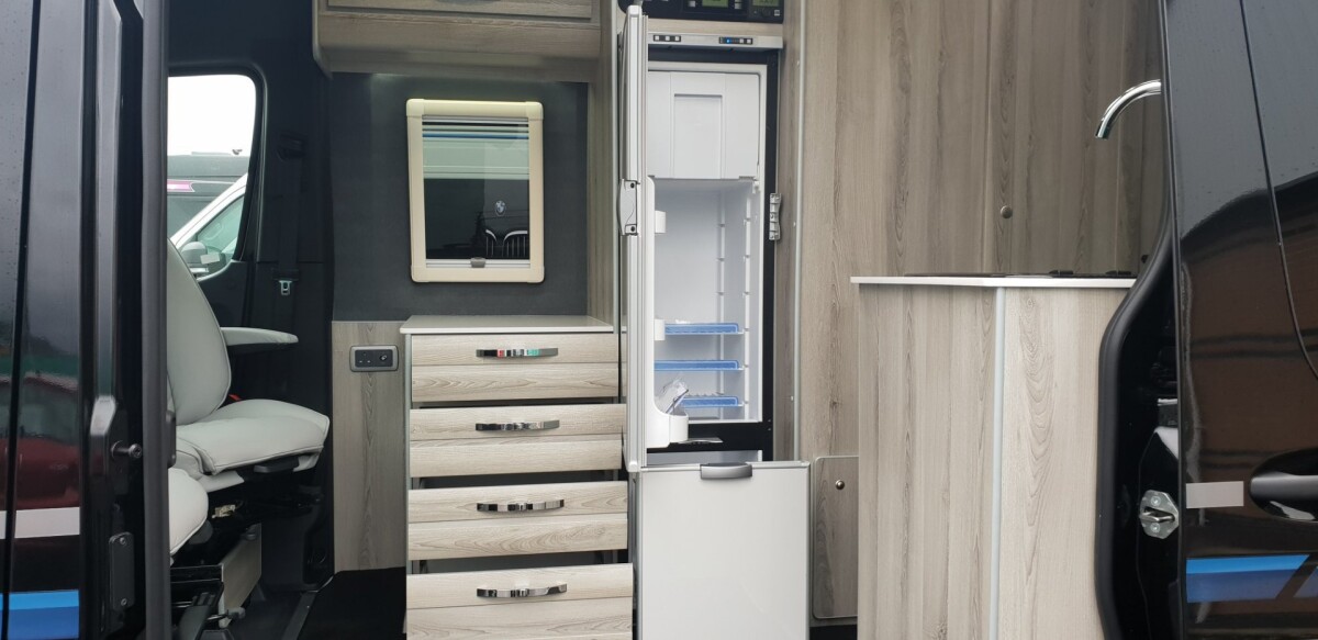 The kitchen straddles the aisle with a 150-L fridge and worktop/drawer unit located across from the main cooktop block
