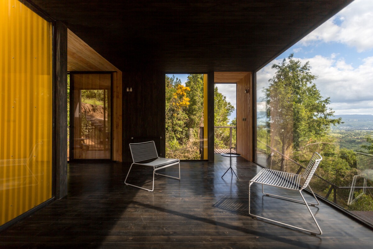 Large floor-to-ceiling glass windows are positioned throughout the entire home, offering stunning views of the surrounding forest landscape