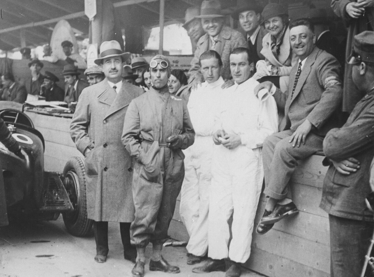 The Scuderia Ferrari Grand Prix Team with Nuvolari the star driver at center, and Enzo Ferrari seated on the pit apron at right