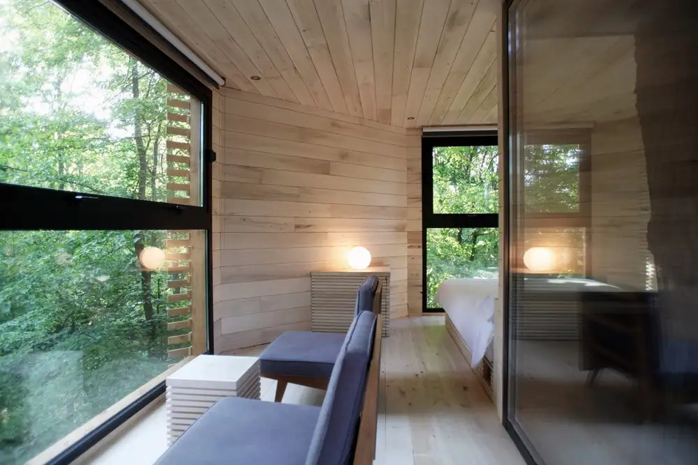 The interior of Origin treehouse, with raw floor-to-ceiling timber cladding, in-built wooden furniture and large glass windows throughout, overlooking the lush treetops