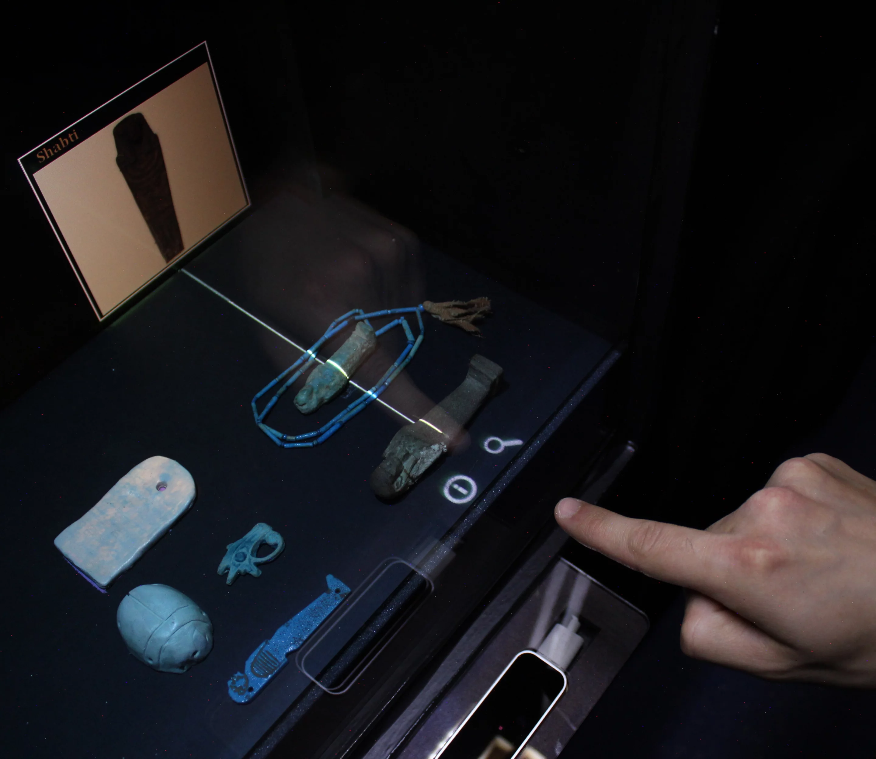 The reflection of a user's finger "touches" a museum artifact, causing a projected pop-up to appear