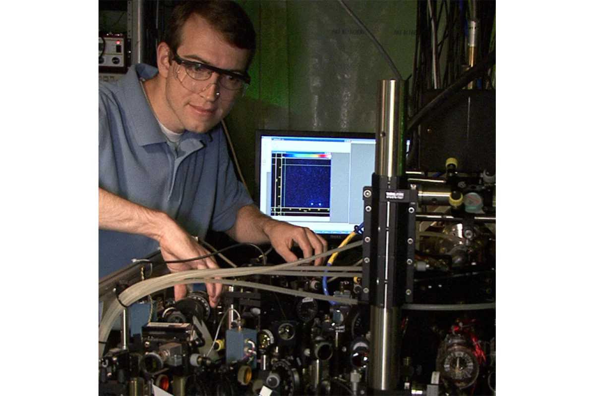 NIST postdoctoral researcher David Hanneke at the laser table used to demonstrate the first universal programmable processor. The monitor displays a colorized image of the two beryllium ions that hold information in the processor (Photo: J. Burrus/NIST)