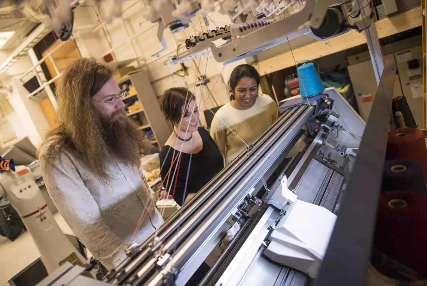 James McCann, Lea Albaugh and Vidya Narayanan watch a knitting machine work on a 3D shape