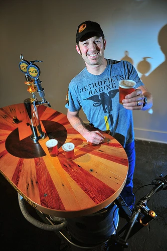 The Beer Bike is a custom-built cargo bicycle that features two beer kegs, a wooden bar with two serving taps, space for pizza boxes, and a solar-powered boom box