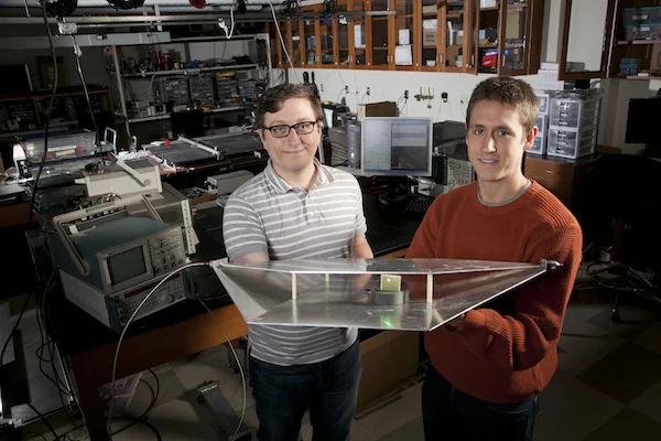 Duke engineering students Alexander Katko (left) and Allen Hawkes show a waveguide containing a single power-harvesting metamaterial cell, which provides enough energy to power the attached green LED